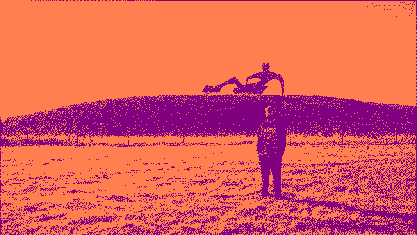 Josh in front of a large, polished brass, abstract sculpture on a small hill. This image has been dithered for stylistic effect.